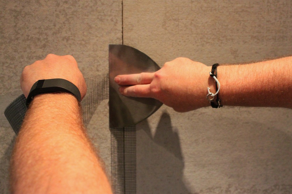 Jamie Uses the BAck of a Putty Knife to Cut the Mesh Tape